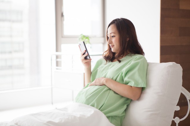 ベットでスマートフォンを見る妊婦さん